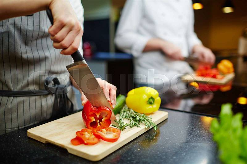 Female in uniform cutting fresh pepper and herbs for salad, stock photo