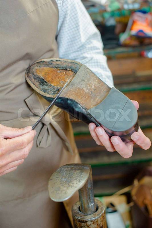 Cobbler scraping sole of shoe with a knife, stock photo