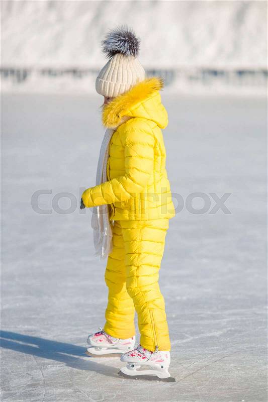 Adorable little girl skating on the ice rink outdoors, stock photo