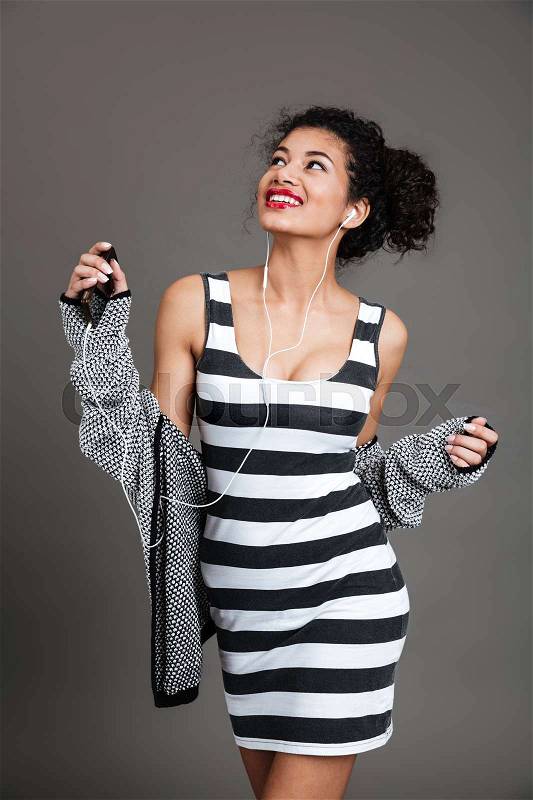 Portrait of a laughing afro american woman with cell phone and earphones isolated on grey background, stock photo