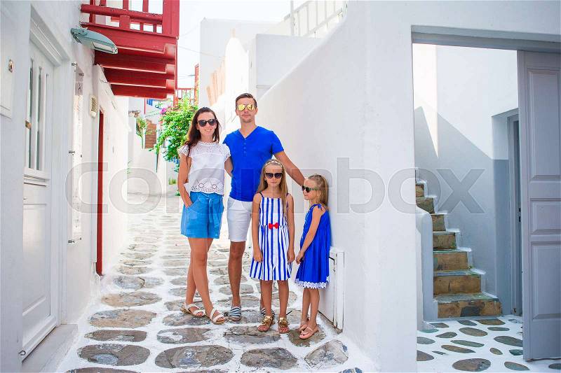 Family vacation in Europe. Parents and kids at street of typical greek traditional village on Mykonos Island, in Greece, stock photo