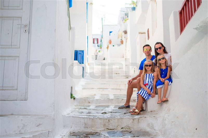 Family vacation in Europe. Parents and kids at street of typical greek traditional village on Mykonos Island, in Greece, stock photo