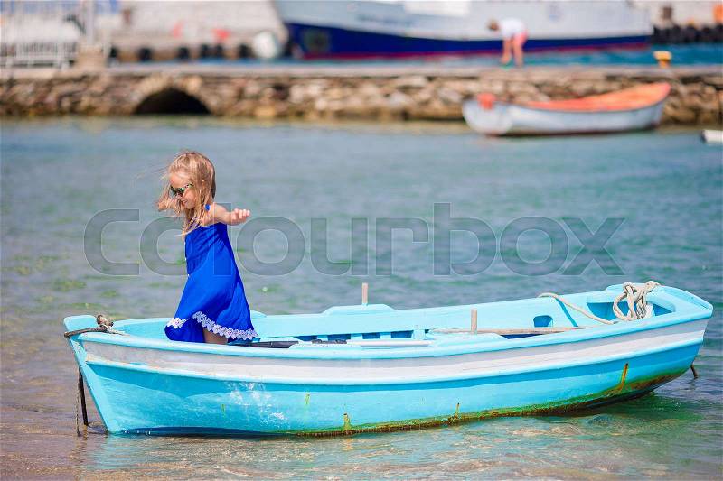 Little girl in blue boat in the sea bay near Mykonos in Greece. Little kid enjoy swimming in the small boat, stock photo