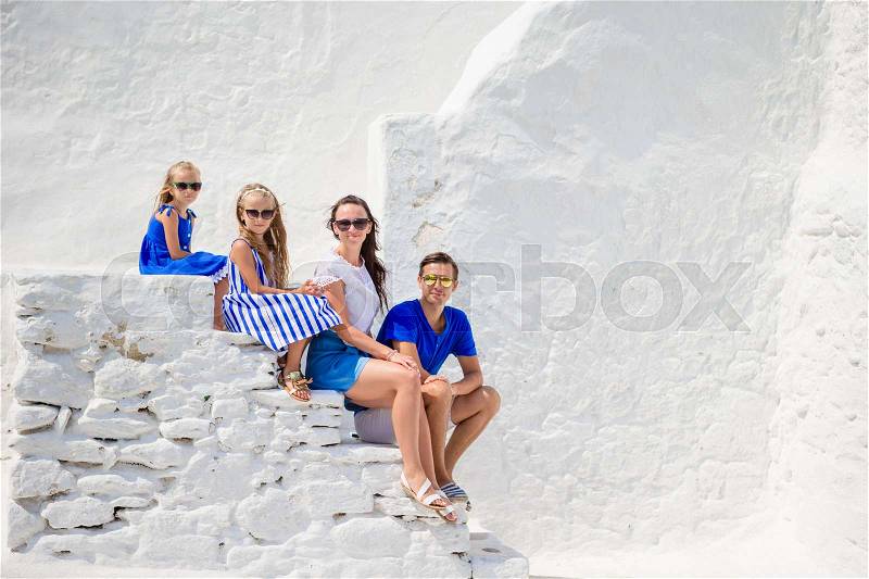 Family vacation in Europe. Parents and kids sitting on the stairs of Paraportiani church on Mykonos Island, in Greece, stock photo