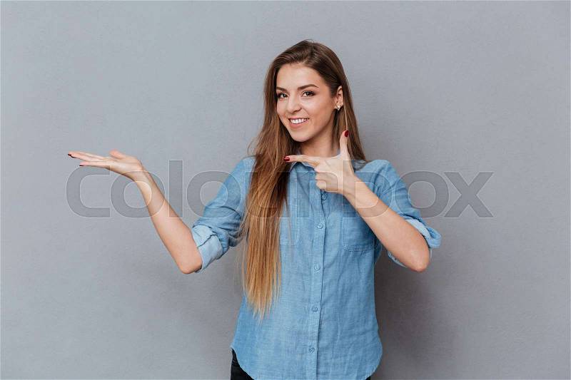 Woman in shirt holding invisible copyspace on the pound and pointing him. Isolated gray background, stock photo