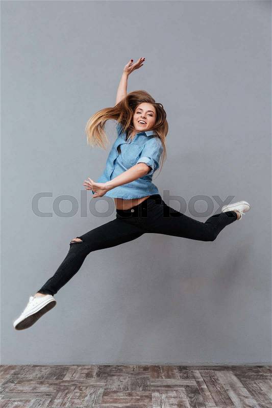 Full length image of happy woman in shirt jumping in studio. Isolated gray background, stock photo