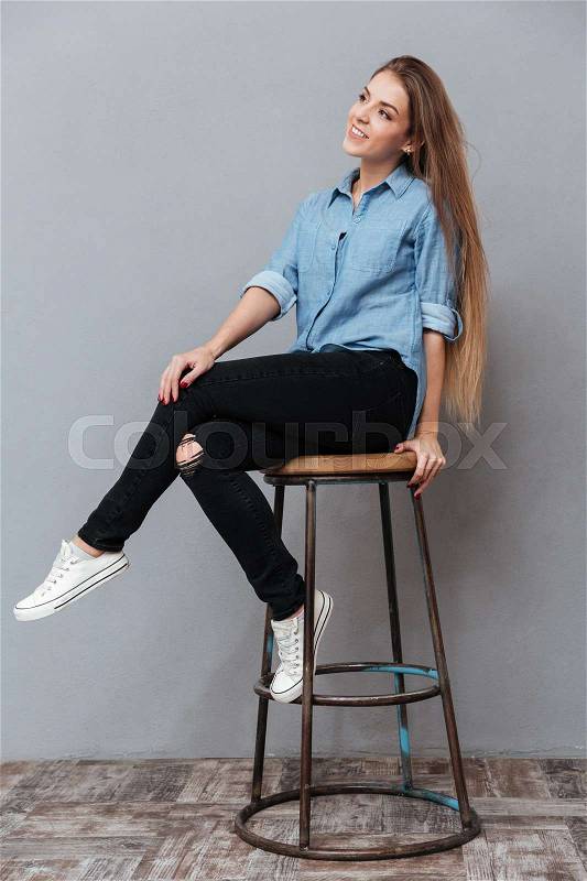 Verical portrait of Woman in shirt posing on chair in studio. Isolated gray background, stock photo