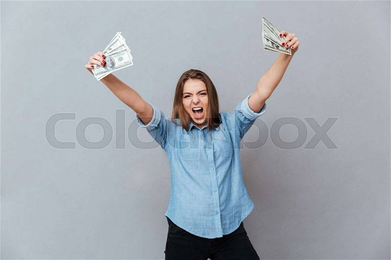 Screaming Happy woman in shirt holding money in hands. Isolated gray background, stock photo