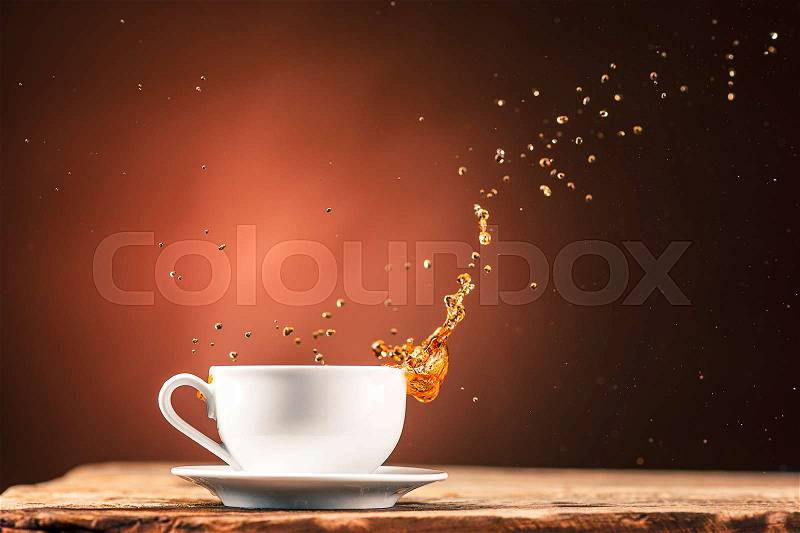 Brown splashes out drink from white cup of tea on a brown wooden background, stock photo