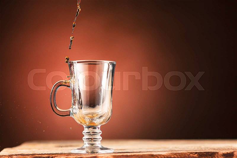 Brown splashes out drink from blue cup of tea on a brown wooden background, stock photo