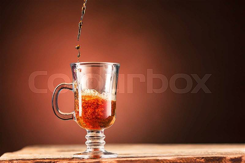 Brown splashes out drink from blue cup of tea on a brown wooden background, stock photo