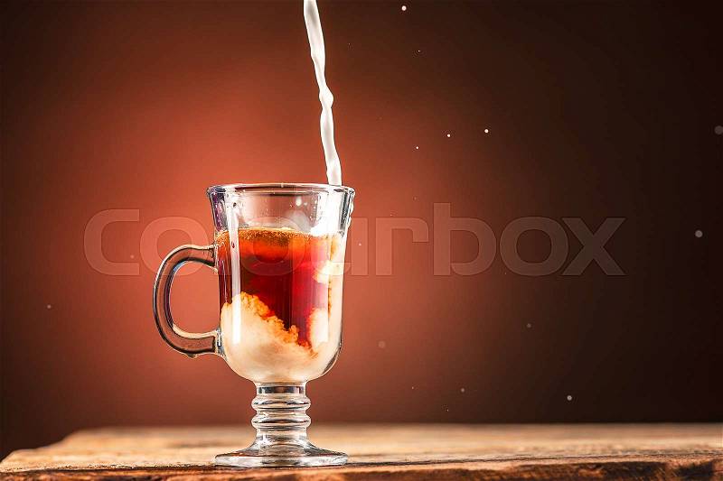 Adding milk to a glass cup of tea on wooden table, stock photo