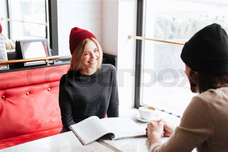Woman in red hat on meeting with her friend sitting by the table in cafe, stock photo