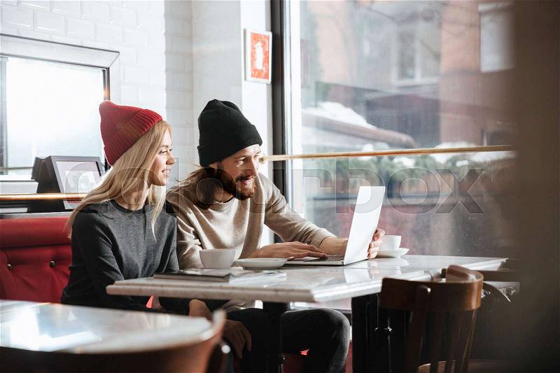 Side view of hipsters with laptop by the table in cafe, stock photo