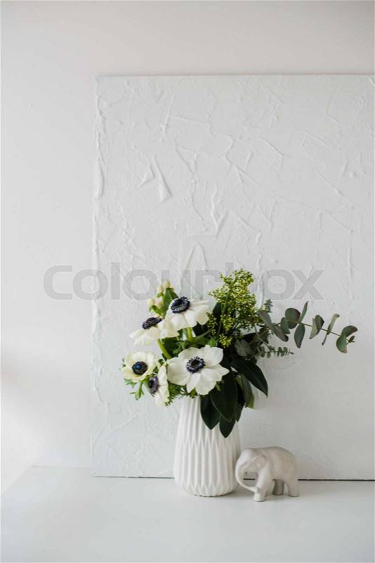 Elegant bouquet of anemones in a vase on table in white room interior, floral home dcoration, stock photo