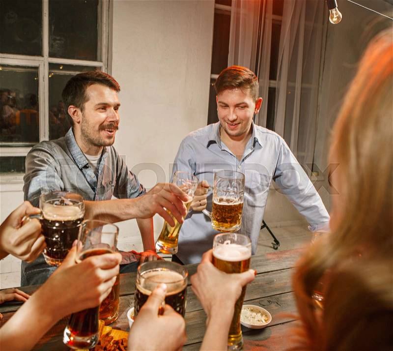 Group of friends enjoying evening drinks with beer on wooden table, stock photo