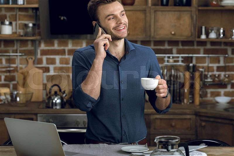 Happy young man talking on smartphone and holding coffee cup , stock photo