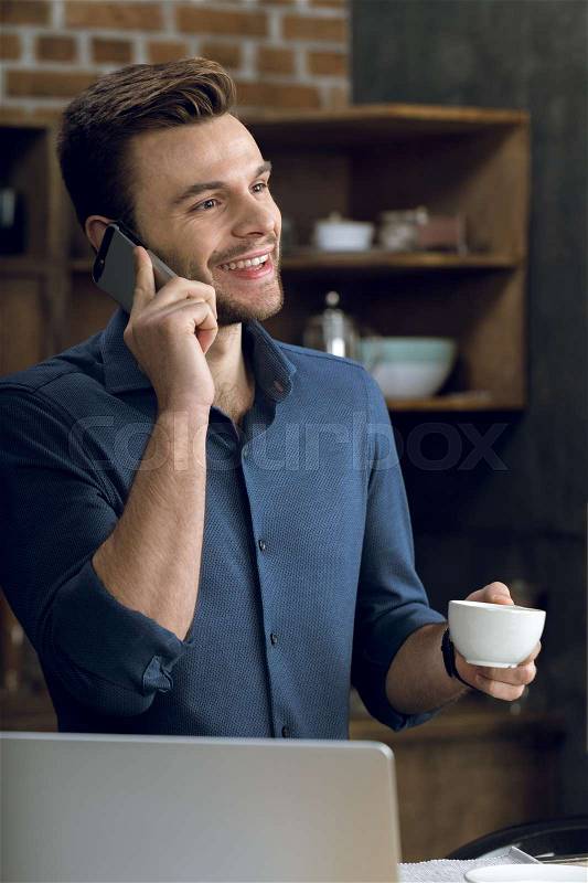 Happy young man talking on smartphone and holding coffee cup , stock photo