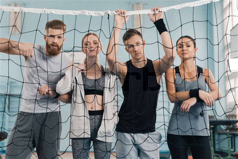Sporty young people looking at camera through net in sports hall , stock photo