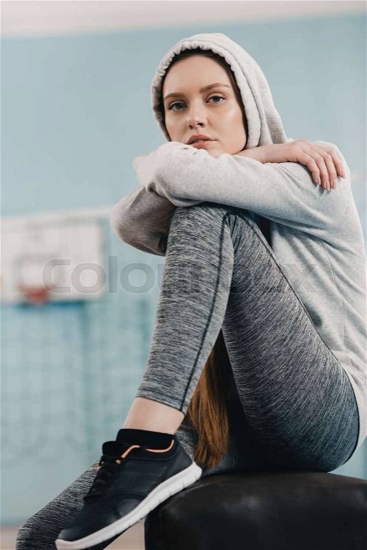 Young sporty woman sitting on pommel horse and looking at camera, stock photo
