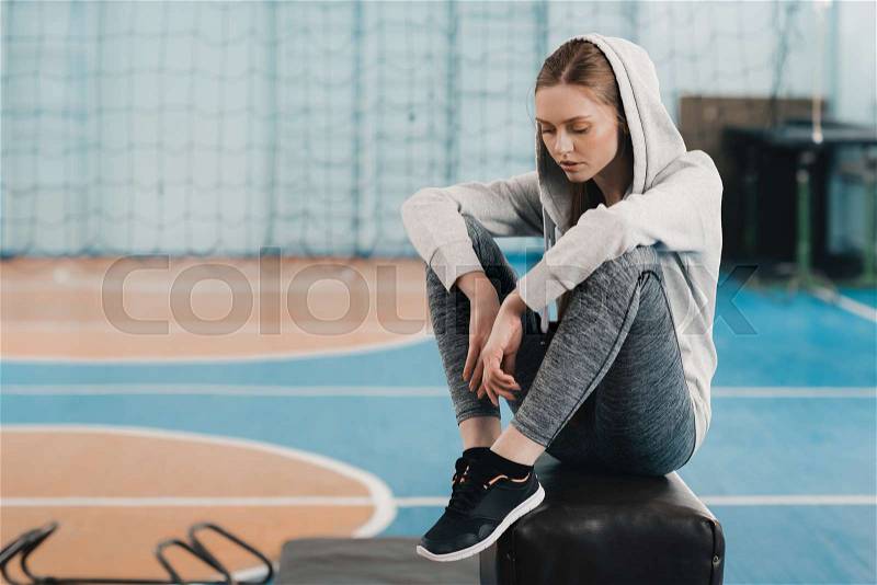 Young sporty woman sitting on pommel horse and looking down , stock photo