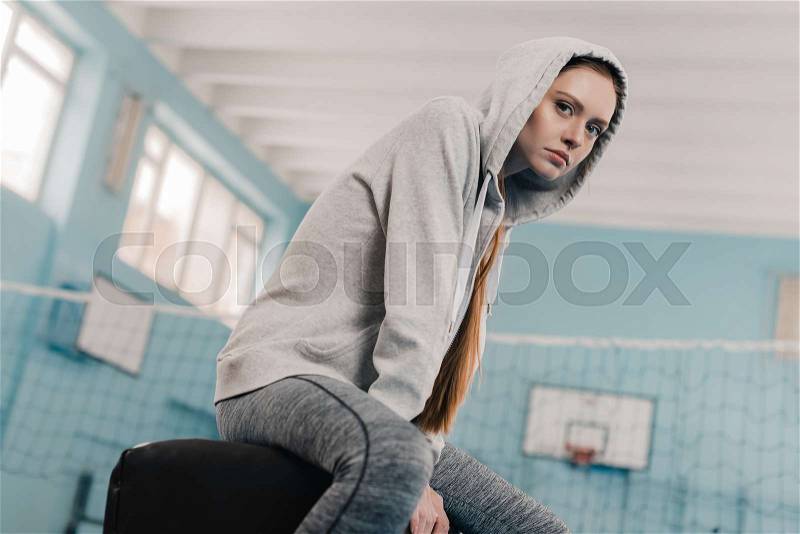 Young athletic woman in sportswear sitting on pommel horse in sports hall, stock photo