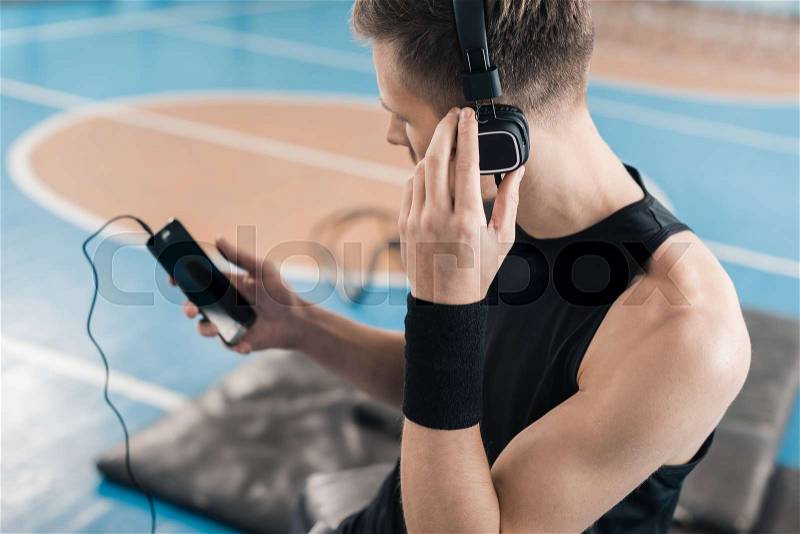Young sportsman in headphones using smartphone in sports center, stock photo