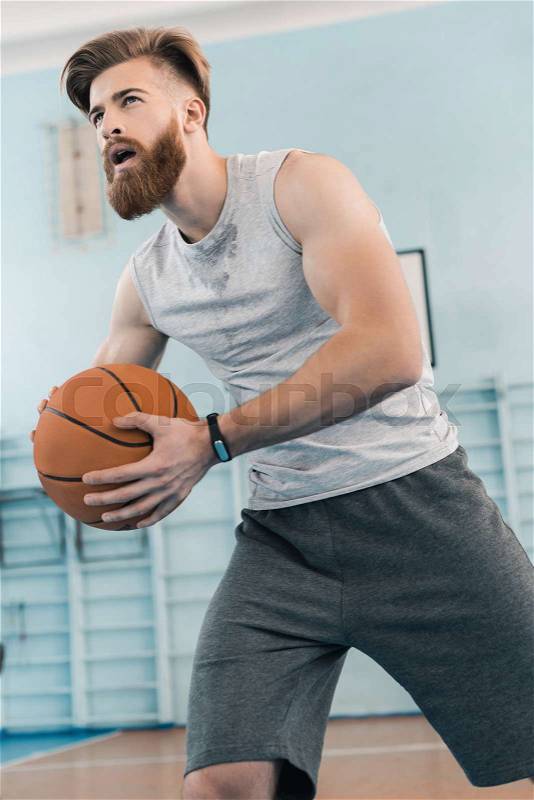 Bearded young athletic man playing basketball in sports center, stock photo