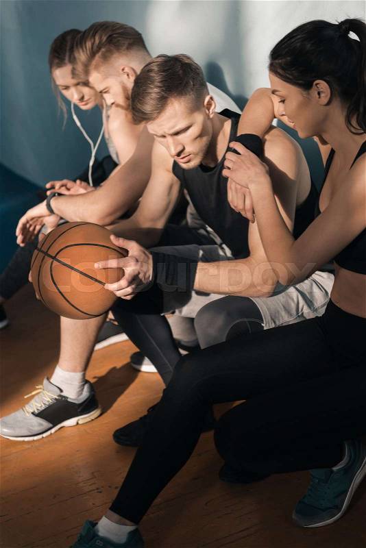 Side view of sporty men and women sitting on bench in gym, stock photo