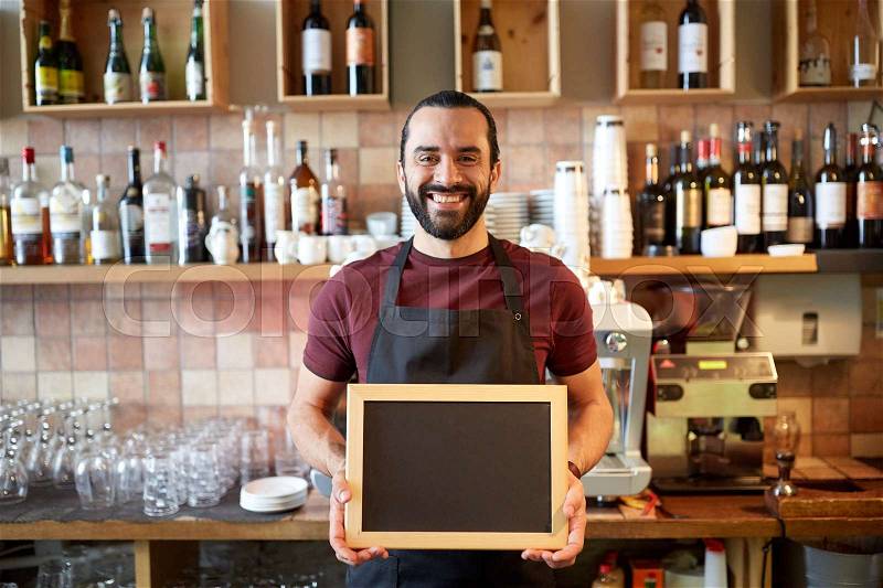 Small business, people and service concept - happy man or waiter in apron with black chalkboard banner at bar or coffee shop, stock photo