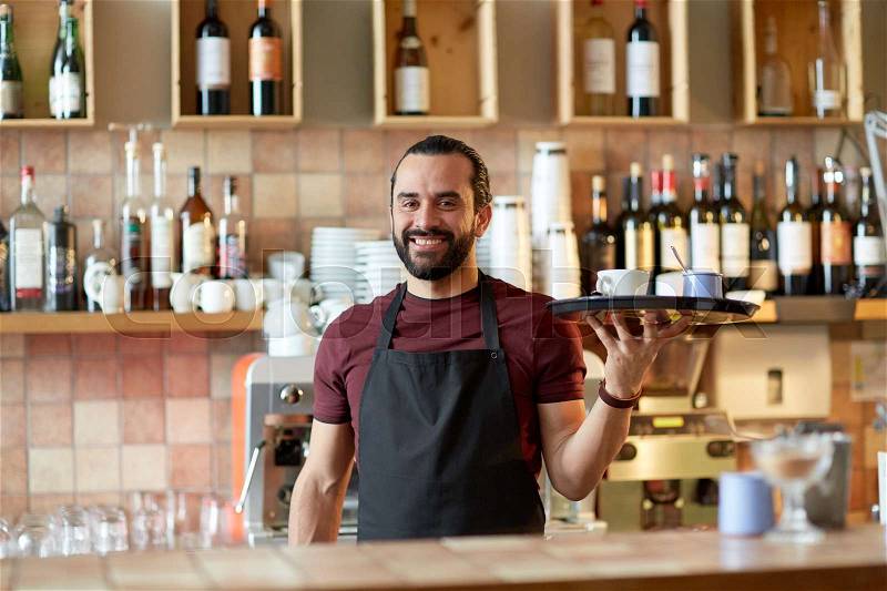 Small business, people and service concept - happy man or waiter in apron holding tray with coffee cup and sugar-bowl at bar, stock photo