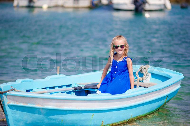 Little girl in blue boat in the sea bay in Greece. Little kid enjoy swimming in the small boat, stock photo