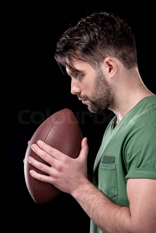 Side view of concentrated man holding rugby ball on black, stock photo