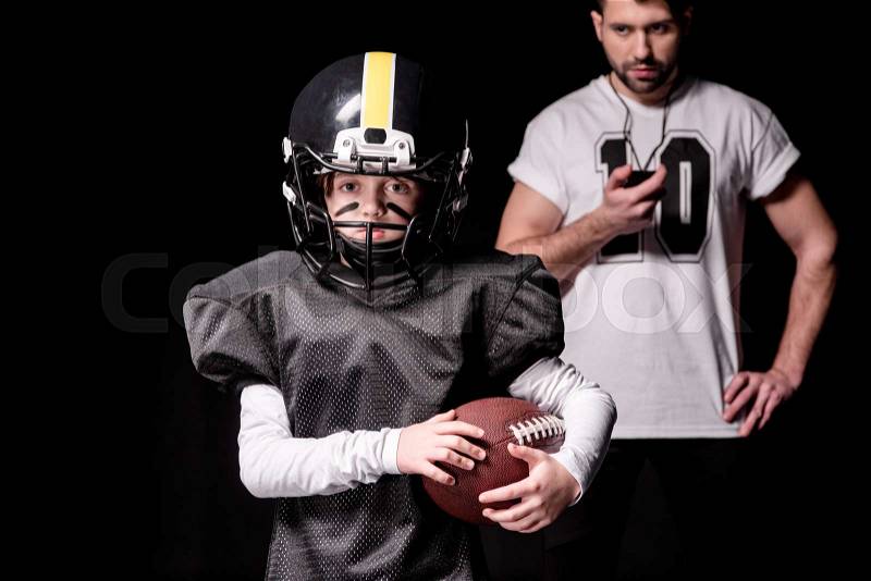 Trainer with sport timer looking at boy american football player on black, stock photo