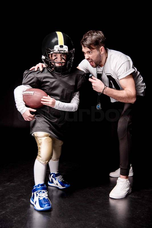 Trainer screaming at boy playing american football on black, stock photo