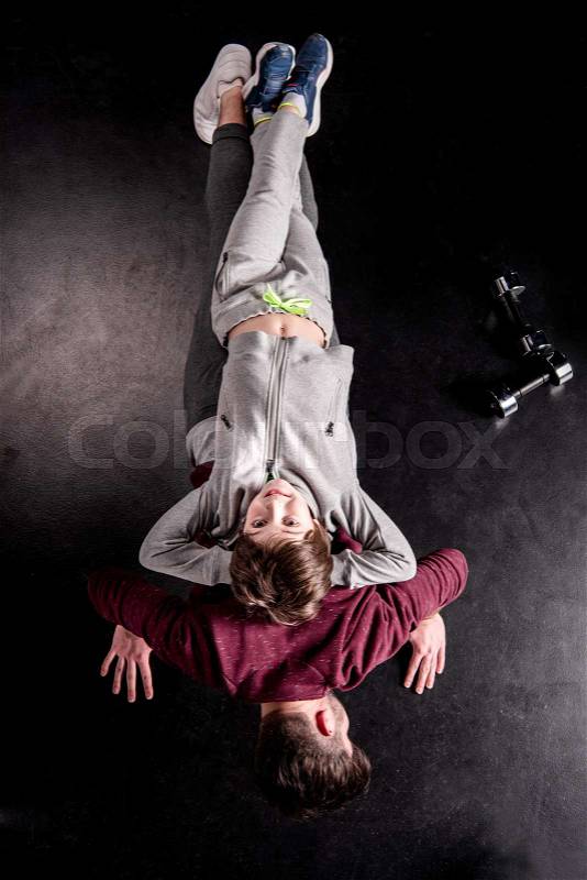 Top view of son lying on back of father doing push ups on black, stock photo