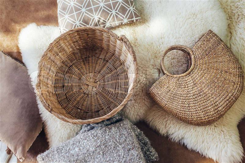 Empty wicker storage basket and handbag, blanket and cushions on sheep carpet, top view from above. Natural and organic interior decor, stock photo