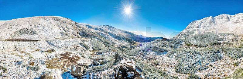 Panorama of white mountains with snow and bright shining sun and sunrays, stock photo