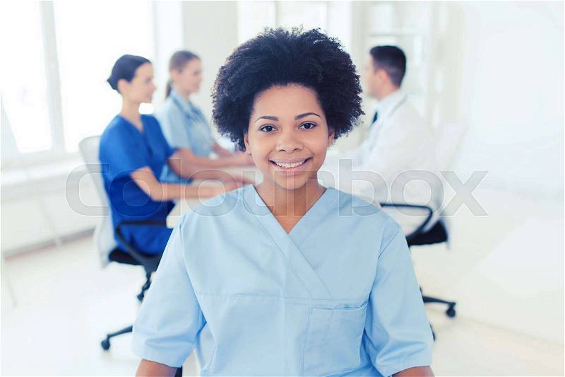 Clinic, profession, people and medicine concept - happy african american female doctor or nurse over group of medics meeting at hospital, stock photo