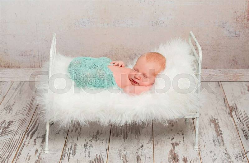 Lovely wrapped newborn sleeping on cot with white soft blanket and toy, stock photo