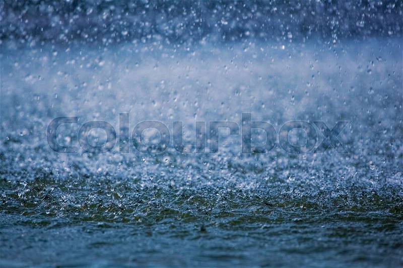 Raindrops running down into a puddle, splashing water visible, stock photo