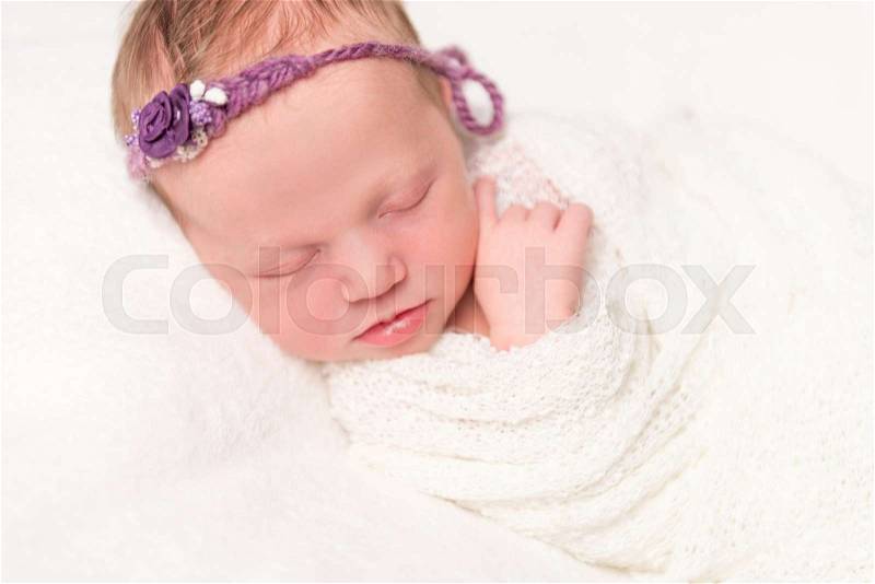 Cute newborn baby in headband with flowers smiling asleep, closeup, stock photo