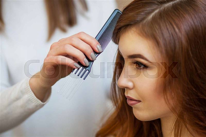 Hairdresser combing her long, red hair of his client in the beauty salon. Professional hair care and creating hairstyles, stock photo