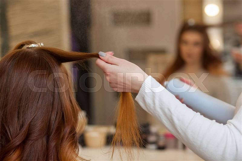Hairdresser combing her long, red hair of his client and sprinkles hairspray in a beauty salon. Professional hair care and creating hairstyles, stock photo