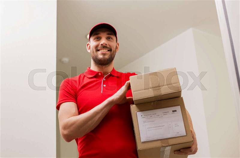Delivery, mail, people and shipment concept - happy man in red uniform with parcel boxes in corridor at open customer door, stock photo