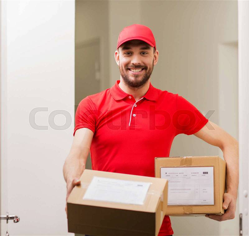 Delivery, mail, people and shipment concept - happy man in red uniform with parcel boxes at open customer door, stock photo