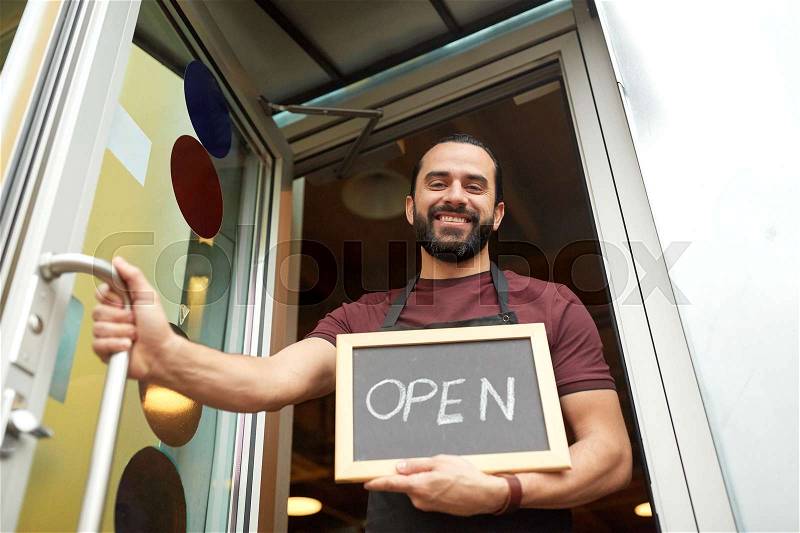 Small business, people and service concept - happy man or waiter with open word on blackboard at bar or restaurant entrance door, stock photo