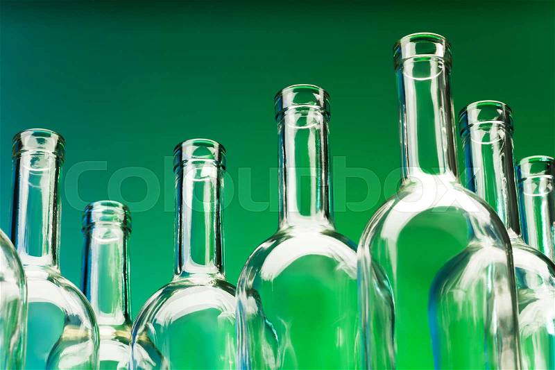 Picture of seven empty wine bottles\' bottlenecks against a green background, stock photo