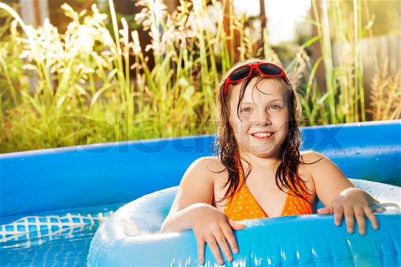 Portrait of happy ten years old girl swimming with blue rubber ring in the inflatable pool, stock photo
