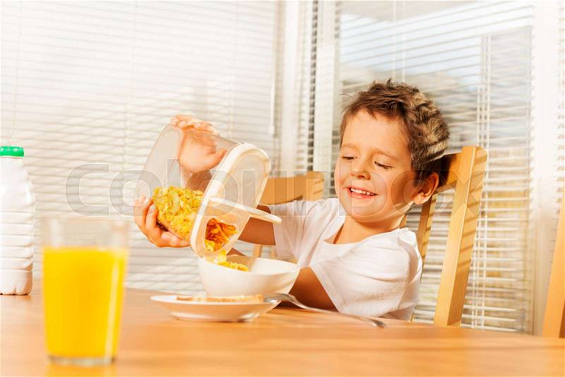 Little boy pouring corn flakes in a plate making cereal breakfast in the kitchen, stock photo